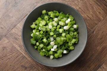 Cut green onion in bowl on wooden table, top view