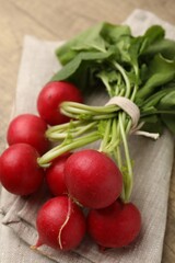 Bunch of fresh radishes with green leaves and napkin on wooden table, closeup