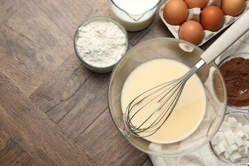 Different ingredients for dough and whisk on wooden table, flat lay. Space for text
