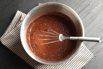 Liquid chocolate dough in bowl and whisk on black table, top view