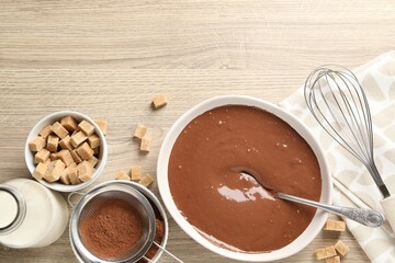 Liquid chocolate dough in bowl, cocoa powder, brown sugar and milk on wooden table, flat lay. Space for text