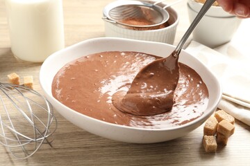 Woman taking liquid chocolate dough with spoon at wooden table, closeup