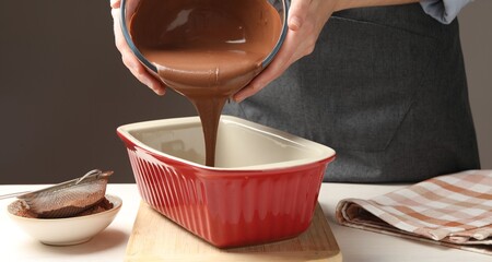 Woman pouring liquid chocolate dough into baking dish at light wooden table, closeup