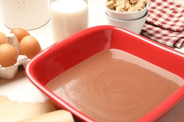 Liquid chocolate dough in baking dish, eggs, brown sugar and milk on white table, closeup