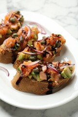 Delicious bruschettas with salmon, avocado, capers, onion and sauce on white marble table, closeup
