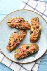 Delicious bruschettas with salmon, avocado, capers and onion on light blue wooden table, top view