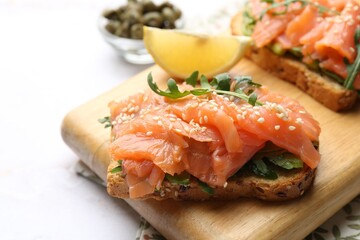 Tasty bruschettas with salmon, arugula, avocado and sesame seeds on white marble table, closeup