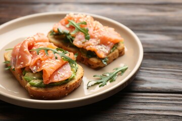 Tasty bruschetta with salmon, avocado, arugula and sesame seeds on wooden table, closeup