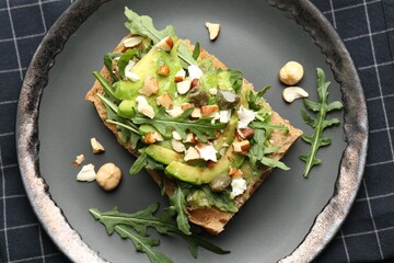 Tasty bruschetta with avocado, arugula, nuts and feta cheese on table, top view