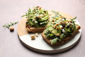 Tasty bruschettas with avocado, arugula, nuts and feta cheese on grey table, closeup