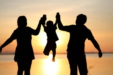 Fototapeta premium Silhouette family holding hands at sunset, reflecting unity, love, and protection. Warm golden light highlights their bond, creating an emotional scene of togetherness, support, and peaceful moments.