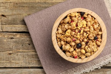 Tasty granola with dried fruits in bowl on wooden table, top view. Space for text