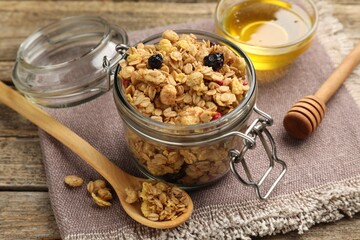 Tasty granola with dried fruits in glass jar and honey on wooden table, closeup