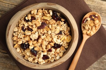 Tasty granola with dried fruits in bowl and spoon on wooden table, flat lay