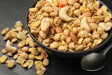 Tasty granola with dried fruits and nuts in bowl on black table, closeup