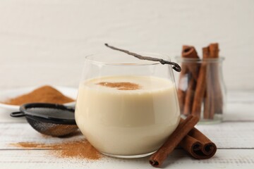 Delicious protein shake in glass, cinnamon and vanilla pod on white wooden table, closeup