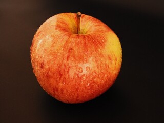 Juicy and delicious red apple with green and yellow spots on a black background