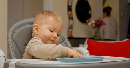 A little boy sits in a high chair, focused on eating fresh fruit for a healthy snack. He appears content while enjoying his meal in a cozy home setting during the afternoon.