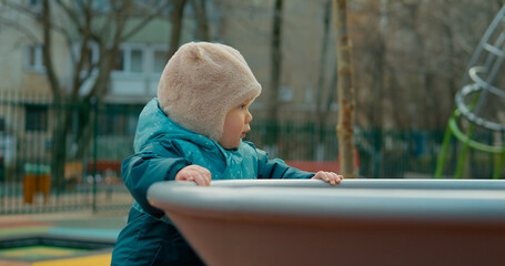 Confident toddler boy developing motor skills while walking independently across playground, wearing warm autumn clothing and exploring surroundings with playful curiosity and joyful expression