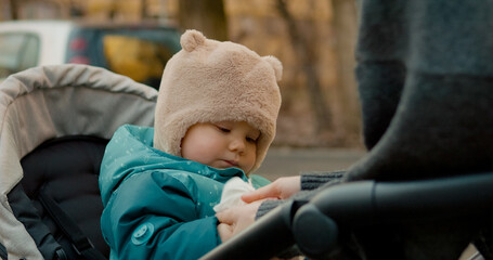 Female gently wipes her baby's hands with a wet wipe while enjoying a leisurely stroll in the park. The child explores the surroundings with curiosity and wonder.