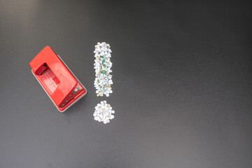 Red heavy duty hole puncher with paper confetti arranged in exclamation mark symbol on black background