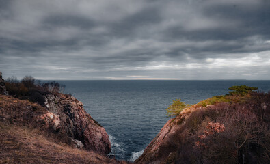 Obraz premium A powerful, high-contrast landscape photograph showing the rugged, reddish-pink granite cliffs of Kullaberg, Sweden, framing a view out to the open sea.