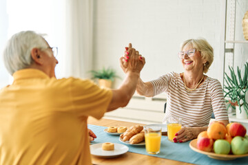 Portrait of an elderly senior couple having breakfast at home. Happy healthy affectionate senior couple eating and sitting at kitchen table having fun enjoying morning meal together