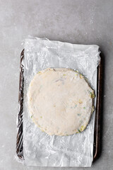 Overhead view of rolled out raw chinese scallion pancakes on parchment lined tray, top view of homemade scallion pancakes, process of making cong you bing
