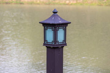 Close-up of an elegant, traditional Chinese-style outdoor pillar light fixture made of black metal and glass, suitable for decorative use in courtyards, pathways, or resort gardens.