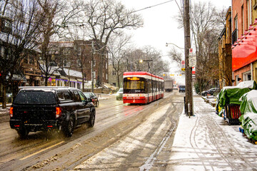 A red Toronto streetcar travels along Queen Street East in the Beaches neighbourhood on a slushy December morning, surrounded by fresh snowfall, wet roads, and passing traffic. Snow-covered sidewalks,
