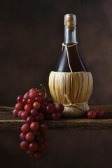Chianti and Grapes Still Life. A bottle of Chianti Wine and a bunch of red grapes draped over the edge of a rustic wood board.