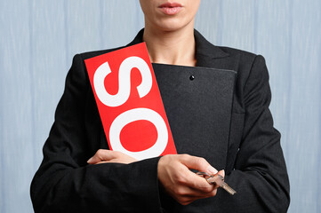 Real estate agent holding out the key to a property whilst clutching a sold sign, close up.