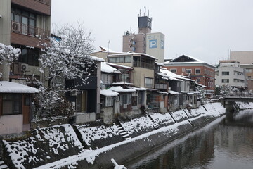 Snow covers old buildings lining a narrow canal in Takayama, Japan