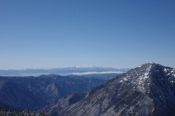 Jagged mountain peak overlooks a sea of clouds and distant snowy ranges.