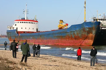 Fotobehang Schipbreuk Many people came to see a small ship washed ashore by a storm.  © VOLODYMYR KUCHERENKO