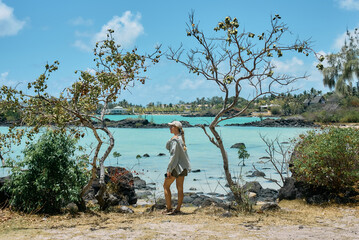 A beautiful woman enjoys spending time on the coastline with a scenic view of a tropical island in Mauritius. The image conveys relaxation, freedom, and a peaceful travel lifestyle