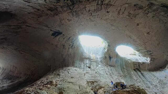 Handheld video from inside Prohodna Cave, filmed upward toward the two ceiling openings known as &ldquo;God&rsquo;s Eyes,&rdquo; with human silhouettes providing scale, 2019