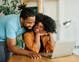 Young happy black couple having fun using a laptop at home