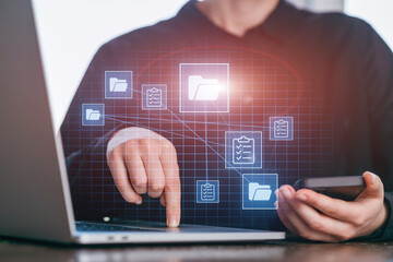 Person using laptop and smartphone to manage files and tasks in a workspace during daytime
