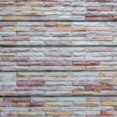 Stacked stone wall texture with multicolored rectangular blocks showing natural rough surfaces and subtle tonal variations, ideal for backgrounds, architectural design, construction material concept.