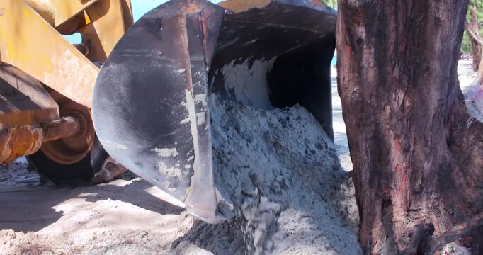 close up of a front end loader pushes a mass of sand along the beach, its metal bucket hard at work.