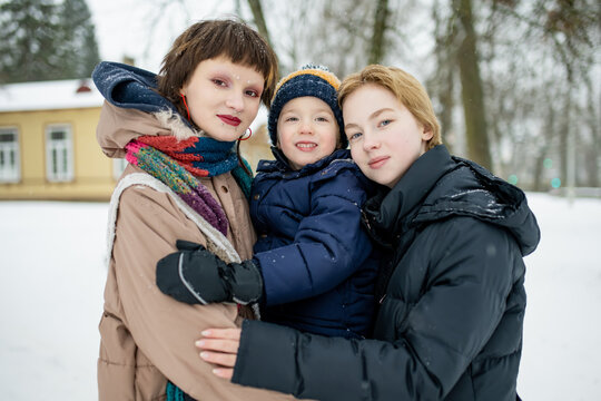 Two teenage girls embrace their younger brother in a snowy park, dressed in winter coats. A tender family moment in cold weather, warmth held close despite the chill. - Powered by Adobe