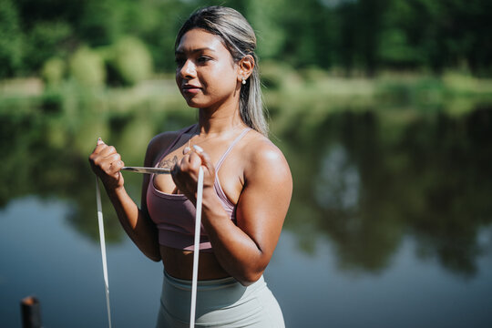 Indian woman exercising with a resistance band outdoors in a natural park setting. Demonstrating focus and fitness, her workout session showcases outdoor activity and prioritizing health and well