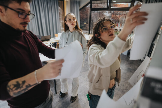 A group of students works together in a bright study space, reviewing papers and a large sheet on a board. They explore ideas, discuss plans, and support each other during a collaborative design