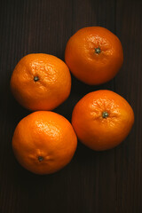 Four fresh clementines in a group on dark wooden table, nutritious delicious fruits for a healthy diet
