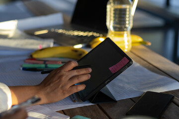Person is actively studying, writing on a digital tablet with a stylus, surrounded by school supplies, a laptop, hydration, and fruit, representing modern education and remote work