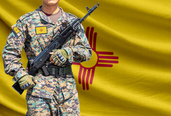 Fototapeta premium New Mexico US state flag with soldier in military uniform holding assault rifle in front of it