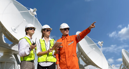 Engineers coordinating at satellite communication facility under clear sky