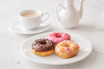 Trio of glazed donuts with coffee cup and pitcher in bright morning light