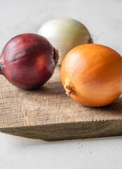 Three whole onions on rustic board showing red, yellow, and white varieties